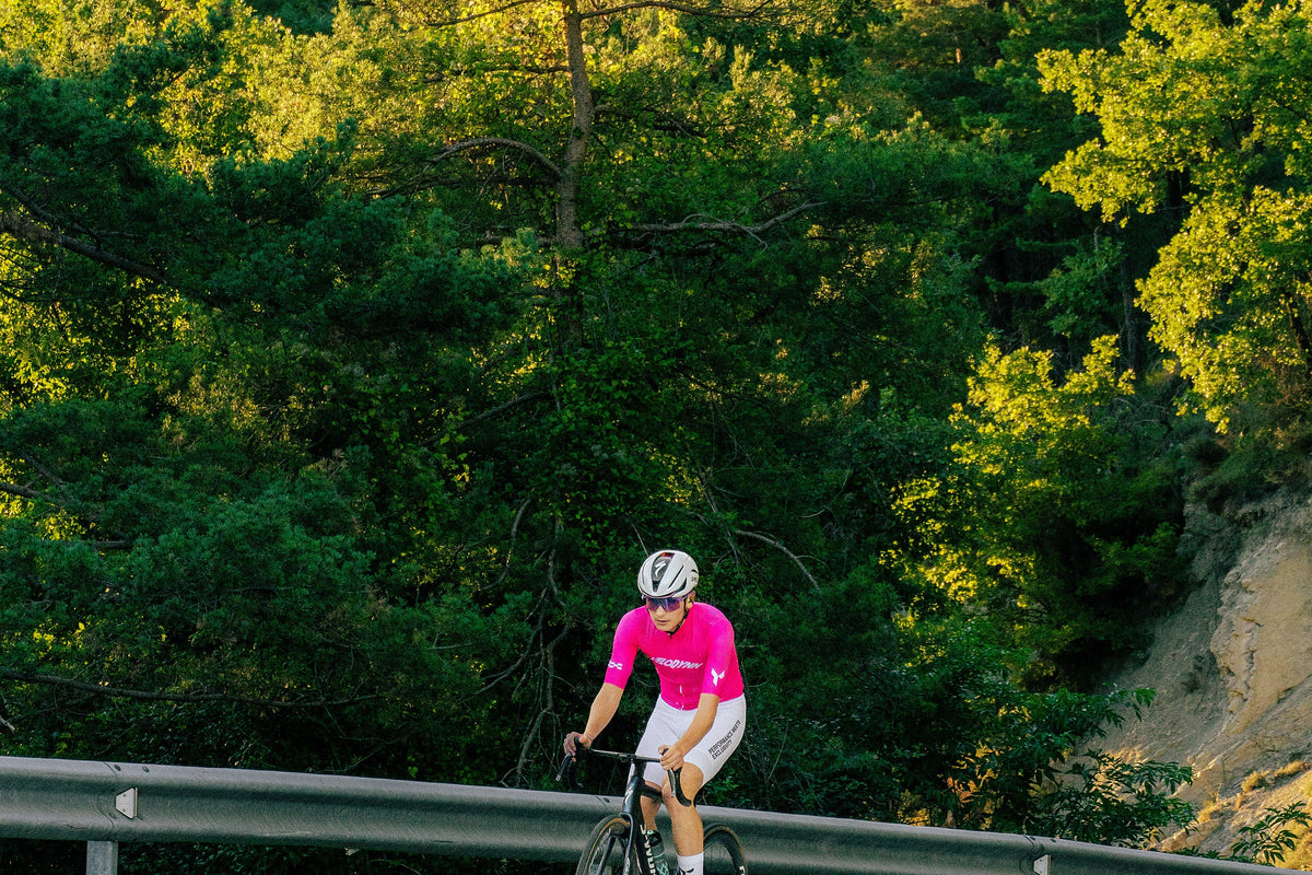 Rider in the pink Ráfaga jersey on a road through the pines at sunset