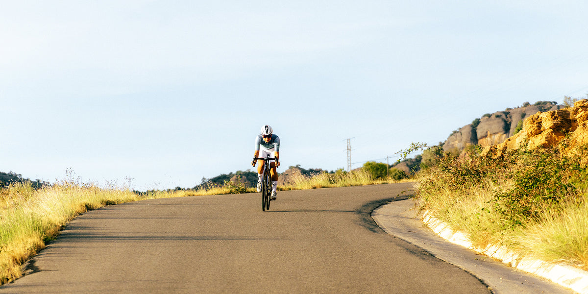 Ciclista que se acerca por una carretera vacía entre rocas y hierba seca
