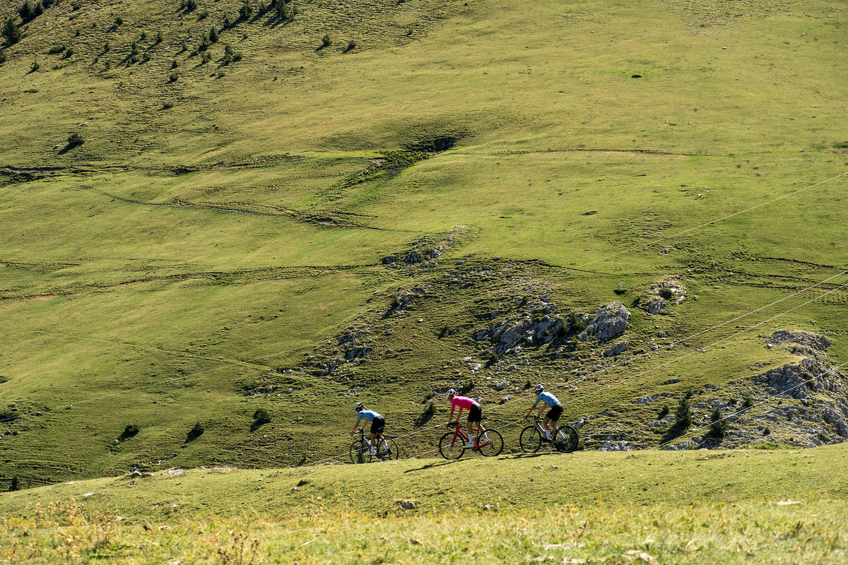 Tres ciclistas cruzando un prado alpino verde