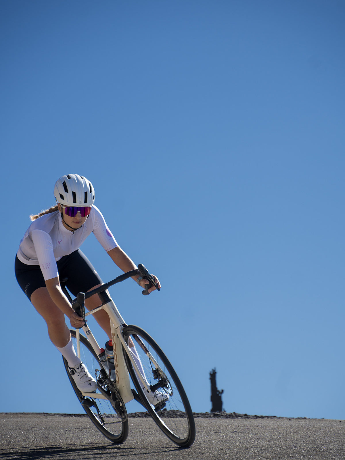 Ciclista con un maillot blanco Velodynn inclinándose en una curva bajo el cielo azul